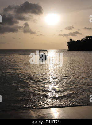 Silhouette kleines Boot verankert unter einer goldenen Himmel weiße Kugel untergehenden Sonne, Nordende Morne Rouge Strand, Grenada, West Indies Stockfoto