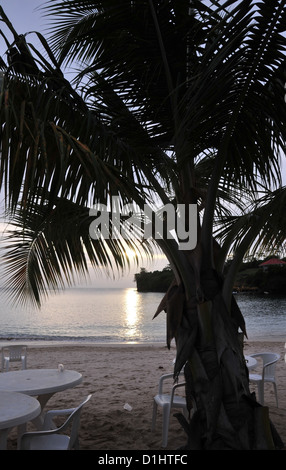 Weißer Kunststoff Tische Stühle unter Silhouette Palme in Richtung Sonne, Gem Resort Morne Rouge Strand, Grenada, West Indies einstellen Stockfoto