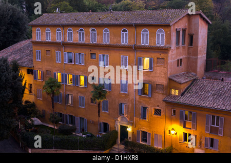 Orange Leuchten Lichter bringen die leuchtenden Farben des Apartment-Gebäudes in Rom, Italien. Palmen im Vordergrund. Stockfoto