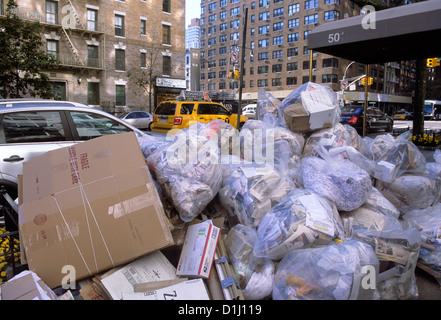 Straßenstandort für die Abfallbeseitigung. Müll in einem Haufen Plastiktüten und einem großen Kartonkarton, der auf einem Bürgersteig in New York City, USA, auf die Abholung wartet Stockfoto