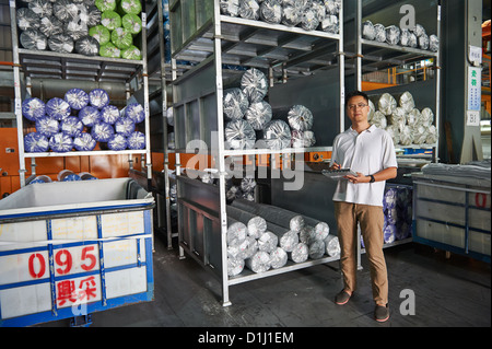 Ein Manager mit einem Klemmbrett steht neben einer Palette der Walze Stoff Stockfoto