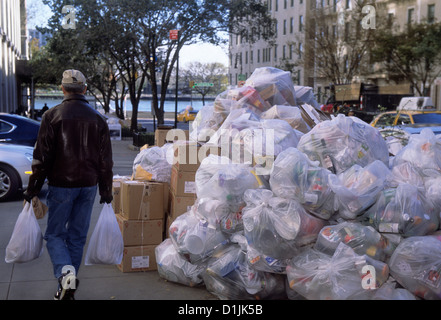 Ein Mann auf der Straße mit Einkaufstaschen geht an einem Stapel von Plastikmülltüten vorbei. Müllentsorgung auf dem Gehweg in New York City Yorkville, USA Stockfoto