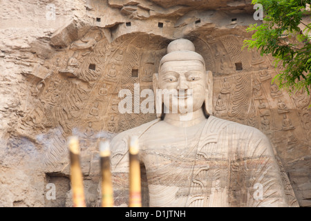 Drei brennende Räucherstäbchen vor einer riesigen Buddhastatue. Der Schwerpunkt liegt auf den Weihrauch. Stockfoto