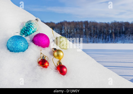 Weihnachten Spielzeug und Silvester-Kugeln im Schnee am Hang eines Hügels liegen. Im Hintergrund ist ein gefrorene Winter-See und Stockfoto