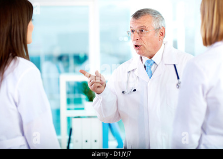 Porträt von Reifen Arzt deutete auf eine der jungen Ärzte während des Gesprächs mit ihr im Krankenhaus Stockfoto