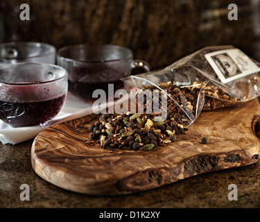 Glühwein Wein Gewürzen verteilt auf ein Schneidebrett mit Glas Tassen gefüllt mit Rotwein im Hintergrund. Stockfoto