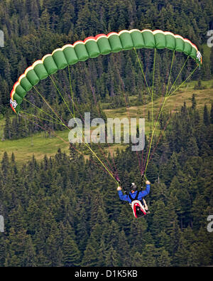 30. Juni 2012 steigt - Girdwood, Alaska, USA - A Gleitschirm im Flug, nach dem Start von der Nordwand des Mt Alyeska, über die hoch aufragenden Fichten in Girdwood Tal sitzt in einem Kabelbaum unter den bunten Stoff Flügel aufgehängt. Mt. Alyeska, der größten Skiberg im Zustand, liegt in Girdwood, Alaska, 27 Meilen (44Â km) von Anchorage, ein Lieblings Startplatz für Gleitschirmflieger. (Kredit-Bild: © Arnold Drapkin/ZUMAPRESS.com) Stockfoto