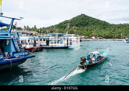 Touristischen Longtailboot geht durch größere verankerte Boote im Hafen von Ban Mae Hat auf Koh Tao im Golf von Thailand Stockfoto