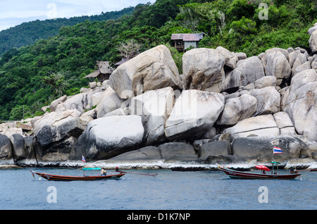 Ein Longtail-Boot mit einem anderen von spektakulären großen Felsbrocken auf Koh Tao im Golf von Thailand. Beide Boote haben Thai Fahnen. Stockfoto