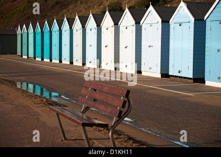 Leere Bank vor einer Reihe blaugrüner Strandhütten an der Promenade zwischen Bournemouth und Boscombe, Dorset UK im Dezember Stockfoto