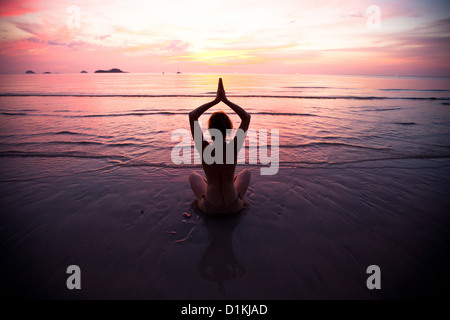Junge Frau praktizieren Yoga am Strand bei Sonnenuntergang Stockfoto
