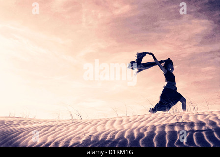 Silhouette einer Frau mit einem wehenden Schal in den Dünen. Stockfoto