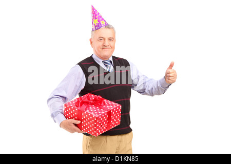 Ein Gentleman mit Partyhut hält ein Geschenk und einen Daumen aufgeben isoliert auf weißem Hintergrund Stockfoto