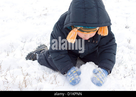 Kleiner Junge sammeln bis Schnee in seinen behandschuhten Händen kniet ein Winter Schneemann oder Schneebälle zu Stockfoto