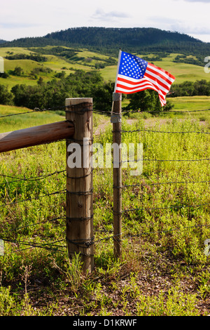 Eine bescheidene amerikanische Flagge mit Klebeband an eine Ranch Zaun in ländlichen Wyoming Snaps im Wind. Stockfoto