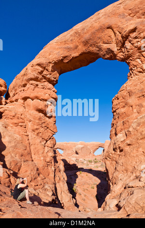 Touristischen saß trinken am Turm Bogen in The Windows Abschnitt Arches National Park in der Nähe von Moab Utah USA Vereinigte Staaten von Amerika uns Stockfoto