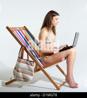 Junge Frau sitzt im Liegestuhl mit einem Laptopcomputer Stockfoto