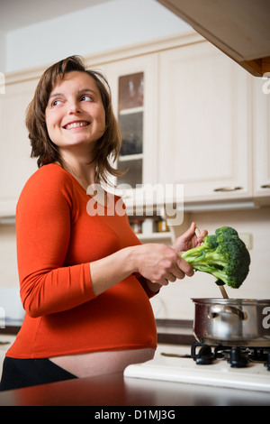 Lifestyle-Porträt von lächelnden schwangere Frau Kochen Brokkoli in Küche Stockfoto