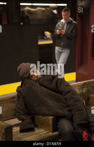 Obdachloser schläft auf einer Bank auf der u-Bahn-Plattform am 34th St. NYC. Stockfoto