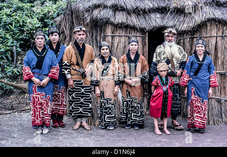 Eine Ainu-Familie indigener Menschen jeden Alters posiert im traditionellen Kleid vor einem Schilf und hetzt auf der Insel Hokkaido im Norden Japans. Stockfoto