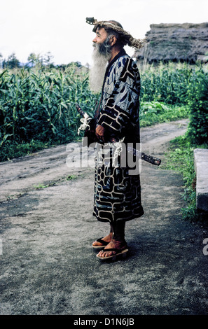 Ein älterer bärtiger Ainu-Mann im traditionellen Kleid und mit seinem zeremoniellen Schwert posiert 1962 außerhalb seiner ländlichen Heimat in Hokkaido, Japan, Ostasien. Stockfoto