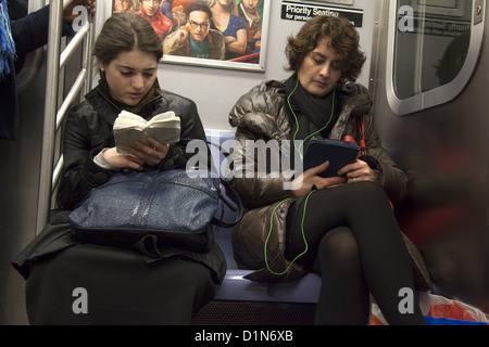 Junge jüdische Frau liest aus ein hebräisches Gebetbuch, während eine andere Frau ihr Tablet in einer u-Bahn Brooklyn, NYC liest. Stockfoto