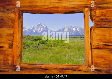 Ein Blick auf den Grand Teton Bergkette von innerhalb des Fensters eine alte Blockhütte. Stockfoto