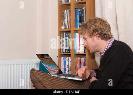 Junger Mann bei Facebook suchen auf einem Laptop auf einen Stuhl im Wohnzimmer zu Hause verlassen einen digitalen Abdruck auf Internet, England, Grossbritannien, Großbritannien Stockfoto