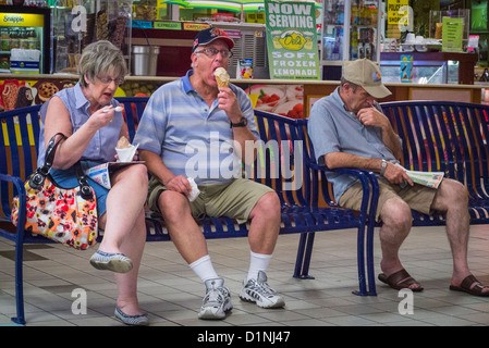 USA Florida USA Florida Boca Raton Flohmarkt Mall im mittleren Alter Menschen in Shorts auf Metall Bank Eis essen Stockfoto