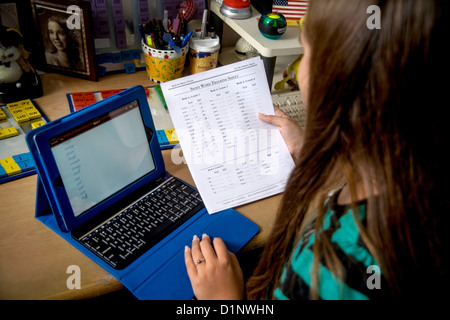 Eine Legasthenie Grundschule Mädchen liest Wörter, die sie versucht hat, auf einem Tabletcomputer von einem Anblick Worte Tracking Blatt zu buchstabieren. Stockfoto