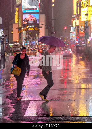 Zwei afroamerikanische Frauen Kreuz Broadway Times Square, New York City, an einem regnerischen Abend. Beachten Sie die beleuchteten Werbeschilder. Stockfoto