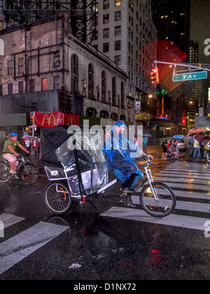 Raincoated Hispanic Rikscha Taxi-Fahrer winkt ein schlägt beim Reiten hinunter Broadway Times Square, New York City. Stockfoto
