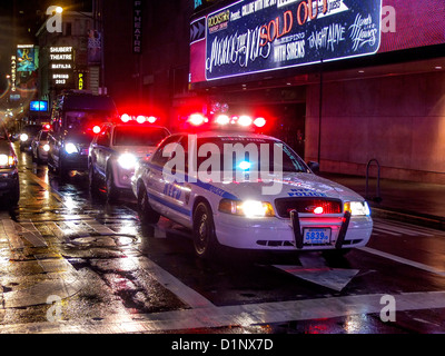 Ein Polizei-Auto-Autokorso begleitet eine Limousine in New York City Times Square Theaterviertel an einem regnerischen Abend. Stockfoto
