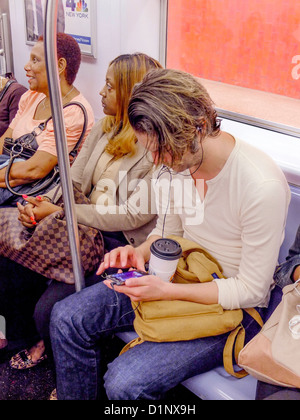 Umgeben von den Passagieren, spielt ein junger Mann ein Computerspiel auf seinem Smartphone während der Fahrt auf der New Yorker u-Bahn. Stockfoto