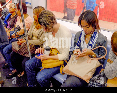 Umgeben von den Passagieren, spielt ein junger Mann ein Computerspiel auf seinem Smartphone während der Fahrt auf der New Yorker u-Bahn. Stockfoto