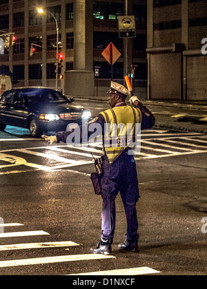 Ein afrikanischer amerikanischer Polizist regelt den Verkehr in der Nacht in New York City in eine Warnweste. Stockfoto