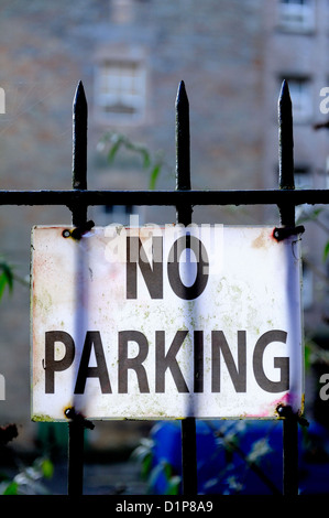 Weißes Kunststoff No Parking Schild angebracht an einen Spitzen Schmiedeeisen Zaun mit Hintergrundbeleuchtung. Stockfoto