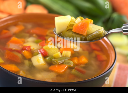 Frische Gemüsesuppe auf Löffel gemacht, der grüne Bohnen, Erbsen, Karotten, Kartoffel, Paprika, Tomaten und Lauch in schwarz Schüssel Stockfoto