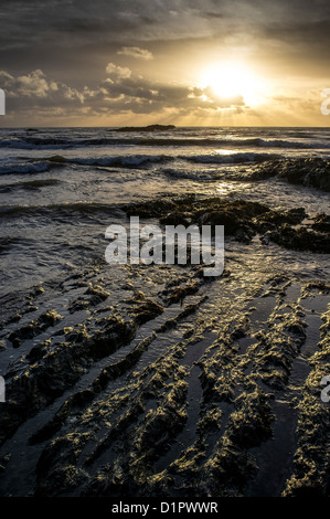 Dramatische Wintersonne, die von einem felsigen Strand über das Meer geht. Ayrmer Cove, Ringmore, South Devon, Großbritannien Stockfoto