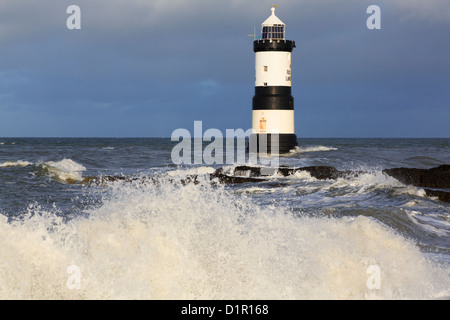 Große Wellen, die an Land mit dem schwarzen und weißen Leuchtturm Penmon (Trwyn Du) vor der Küste an der wilden Küste auf der Penmon Point Insel Anglesey North Wales UK abstürzen Stockfoto