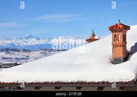 Aus rotem Backstein-Kamin auf dem Dach von Schnee bedeckt und schneebedeckte Berge im Hintergrund unter blauen Winterhimmel im Piemont, Northern Stockfoto