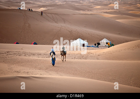 Marokko, M' Hamid, Erg Chigaga Dünen. Wüste Sahara. Kameltreiber, Kamel-Karawane und Touristen verlassen Camps, biwakieren. Stockfoto