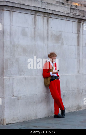 Junger Mann verkleidet als Weihnachtsmann auf seinem Handy, Trafalgar Square, London, Vereinigtes Königreich konzentriert Stockfoto