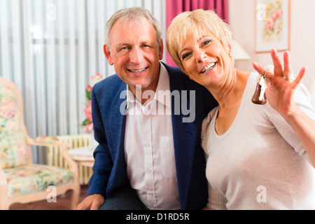 Senior paar sitzt auf dem Bett im Hotelzimmer und die Frau hat einen Schlüssel in der hand Stockfoto