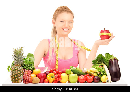 Eine Frau hält einen Apfel umhüllt mit Maßband auf einem Tisch voller Obst und Gemüse isoliert auf weiss Stockfoto