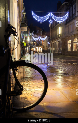 Fahrrad auf Trinity Street in Cambridge in der Nacht. Weihnachtsbeleuchtung auf nassem Asphalt reflektiert. Stockfoto