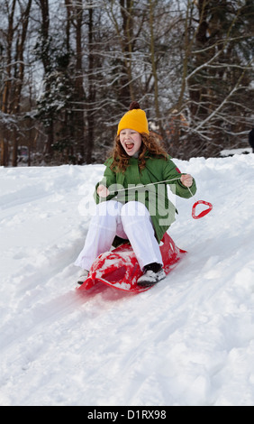 Mädchen Rutschen bergab auf rotem Kunststoff Schlitten in einem verschneiten Winter park Stockfoto