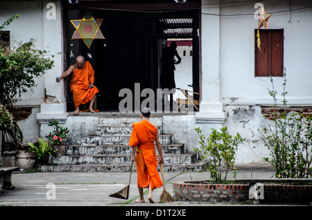 LUANG PRABANG, Laos – buddhistische Mönche und Novizen in hellen Safrangewändern spazieren in einer einzigen Datei durch die Straßen von Luang Prabang während der frühen Morgenzeremonie, bekannt als Tak Fledermaus. Einheimische und Touristen säumen die Strecke und bieten Speisen in diesem täglichen Ritual an, das im Zentrum der buddhistischen Tradition Laos steht. Stockfoto