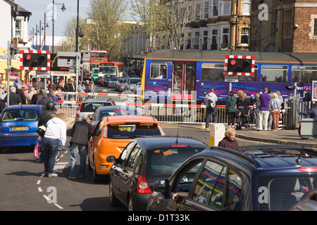 Bahnübergang mit Schranken unten, Zug auf der Durchreise und Schlange von wartenden Verkehr in Paignton, Devon Stockfoto