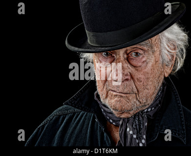 Suche alte Mann mit einem schwarzen Mantel, grauen Schal und schwarze Melone starrte direkt in die Kamera, die isoliert auf schwarz Vintage Stockfoto